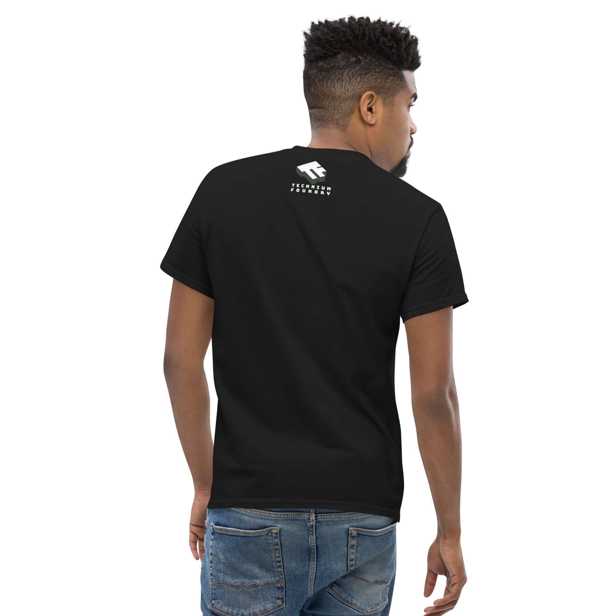Back view of a man wearing a black t-shirt with a small logo near the neck, paired with blue jeans on a white background.