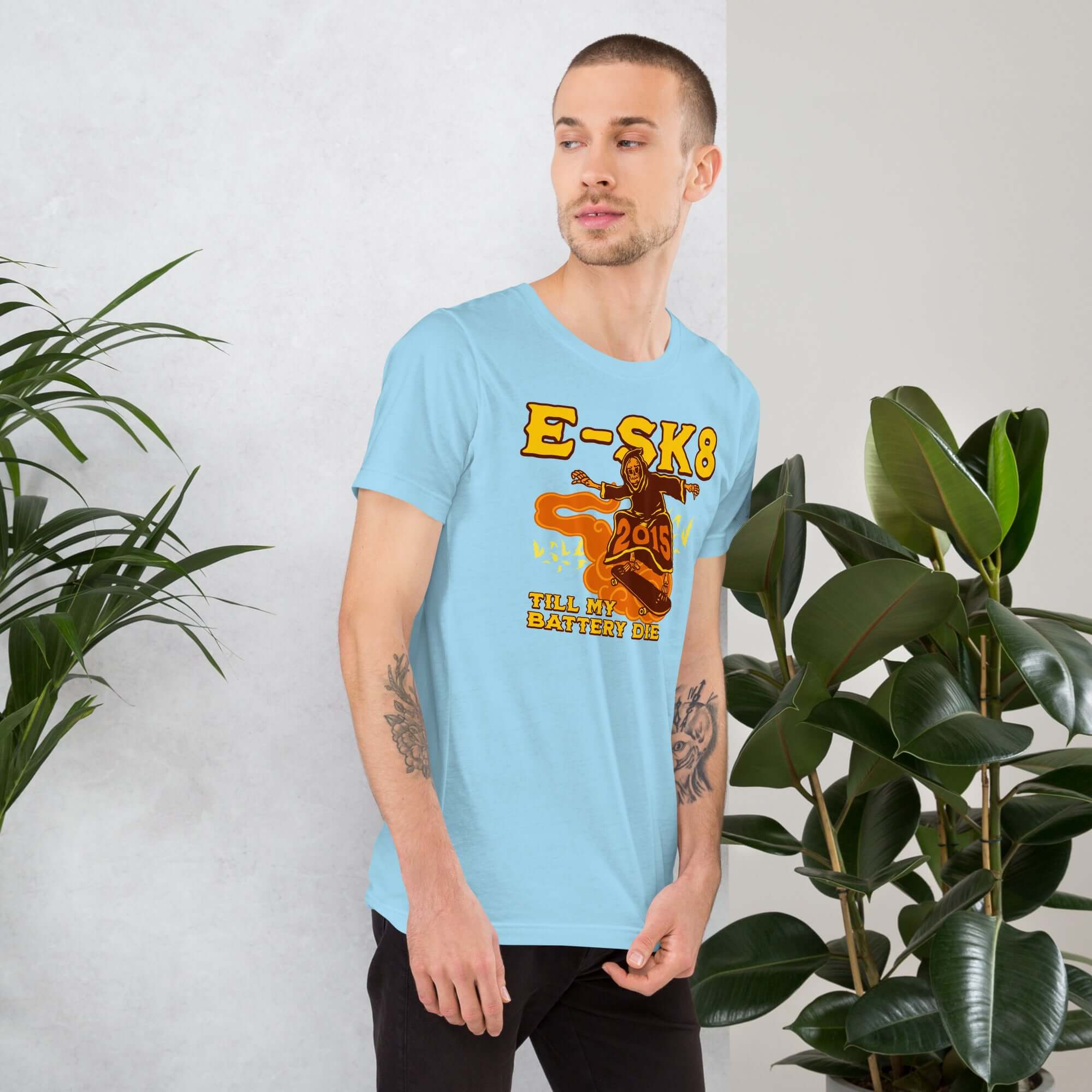 Man wearing E-SK8 Till My Battery Dies T-Shirt with Grim Reaper graphic, standing by plants.