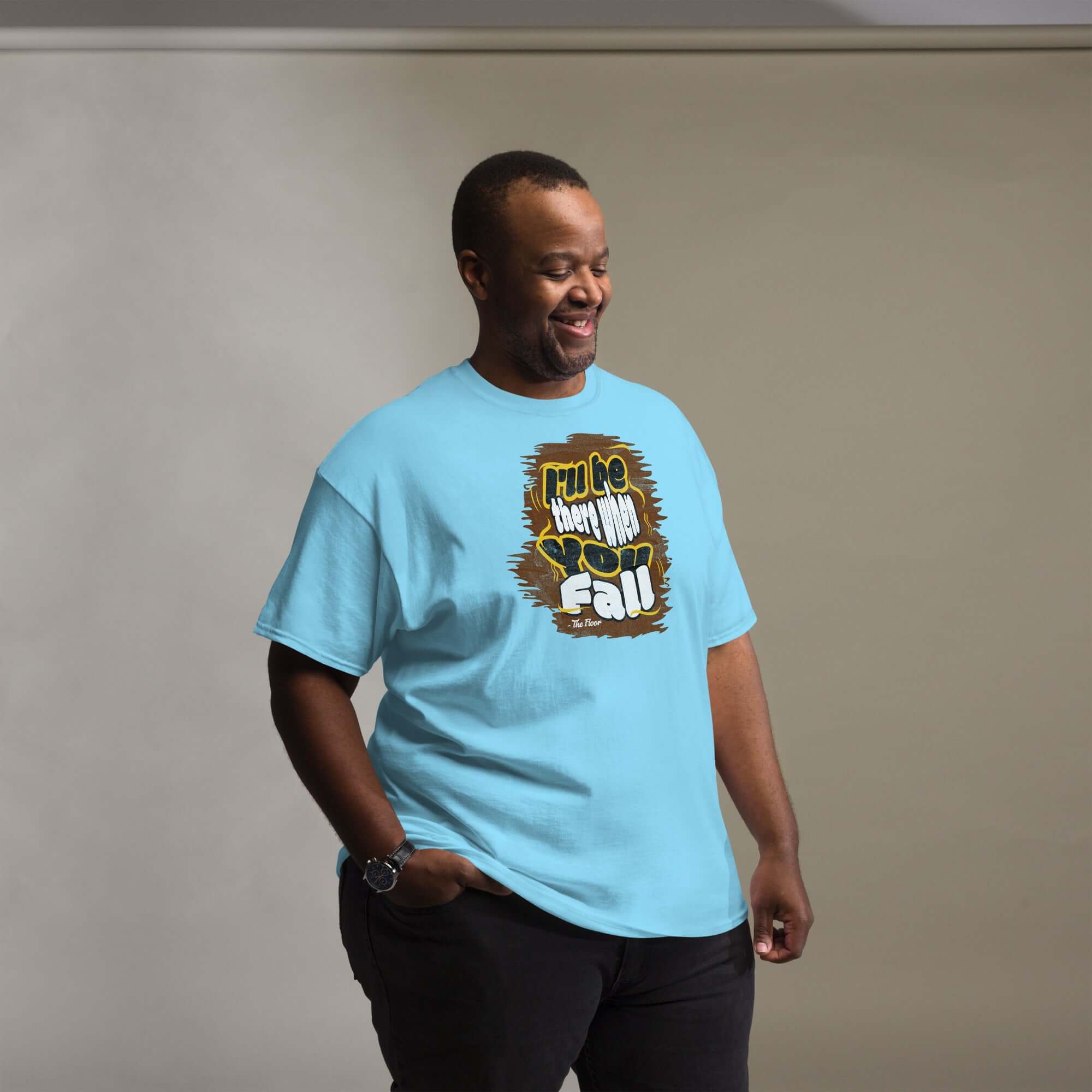 Man wearing blue "I'll Be There When You Fall Floor" ironic t-shirt, showcasing honest humor with bold text design.