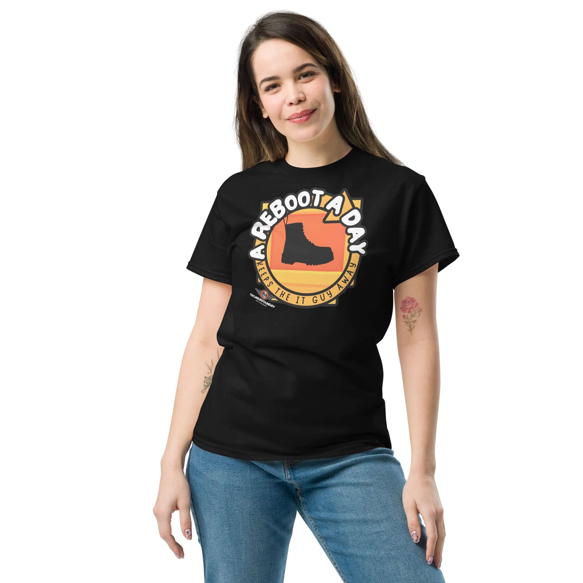 A woman wearing a black "A Reboot A Day" IT support humor t-shirt with combat boot design and sunset backdrop.