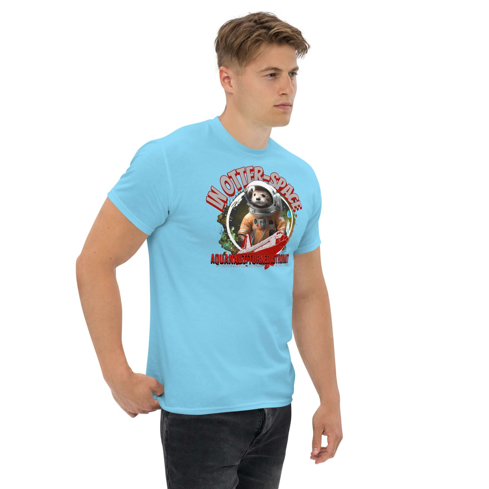 Man wearing blue t-shirt with otter astronaut design, "In Otter Space: Aquanaut Turned Astronaut", cosmic background, orange spacesuit.