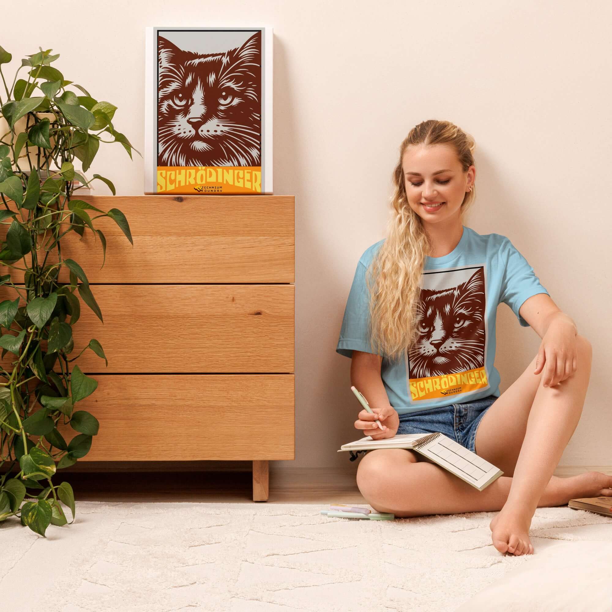 Woman wearing Schrödinger's Cat T-Shirt with retro cat design, sitting next to matching framed art, enjoying a relaxed moment at home.