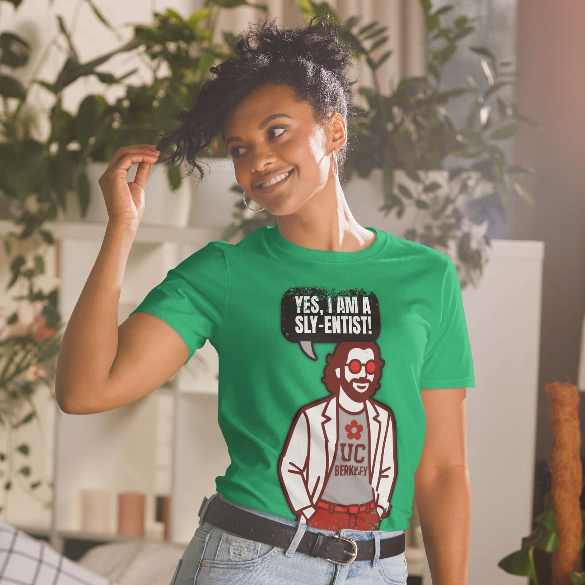 Woman wearing green 'Yes, I Am A Sly-entist' t-shirt with cartoon clown scientist at home.